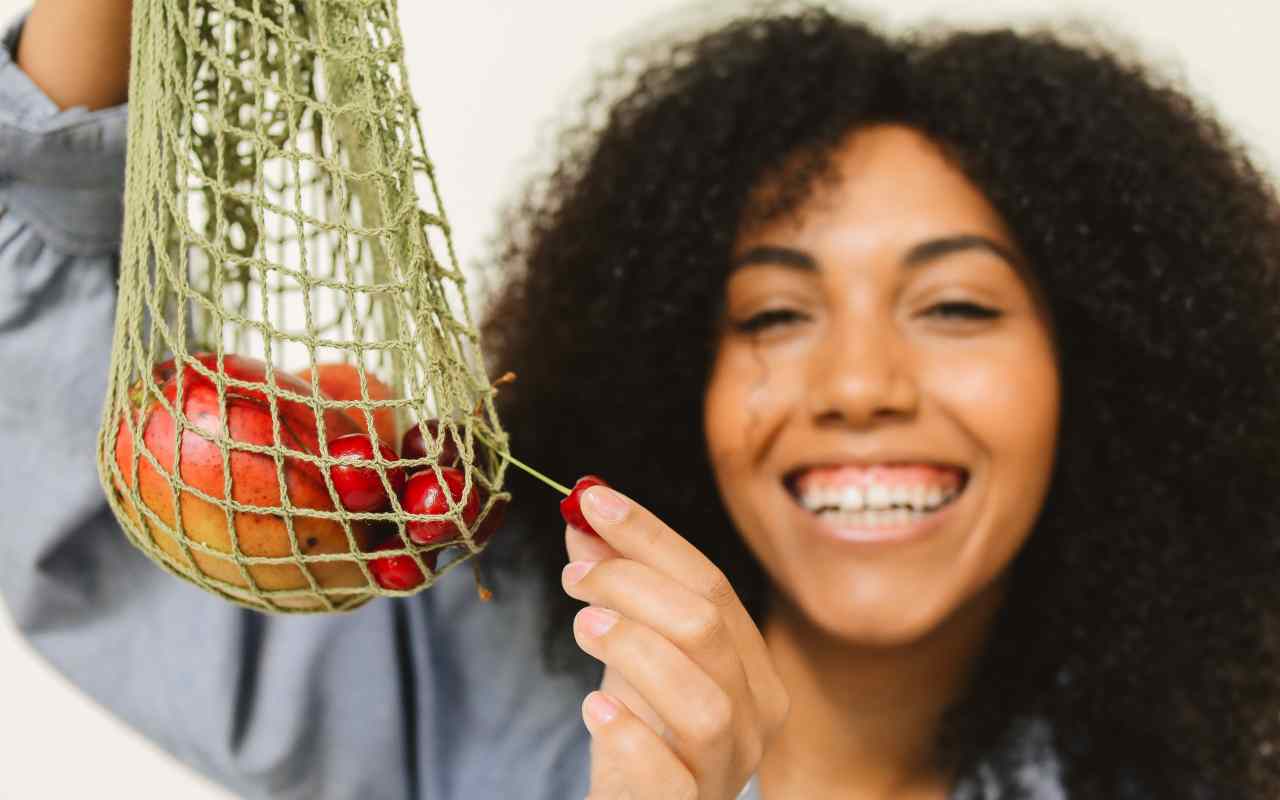 Donna di colore riccia con in mano una rete contenente frutta
