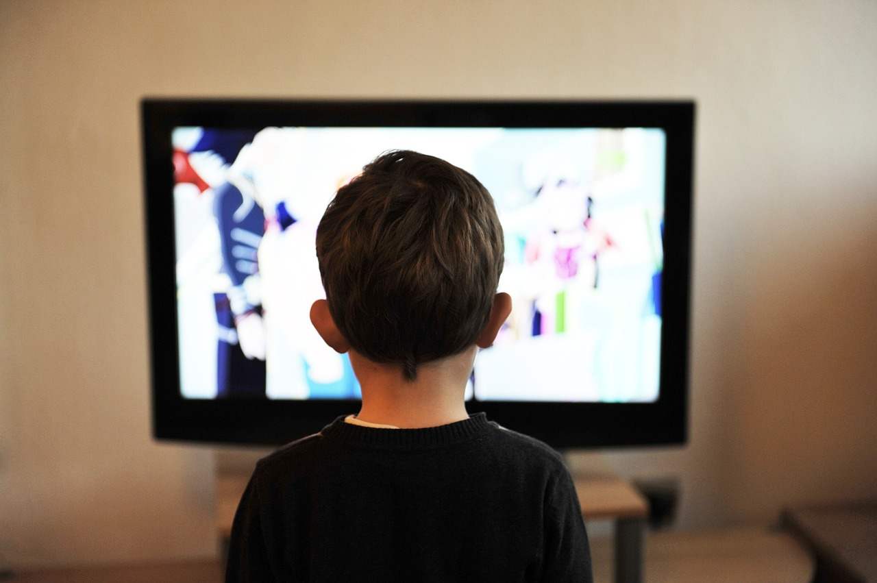 Un bambino di spalle guarda una tv accesa
