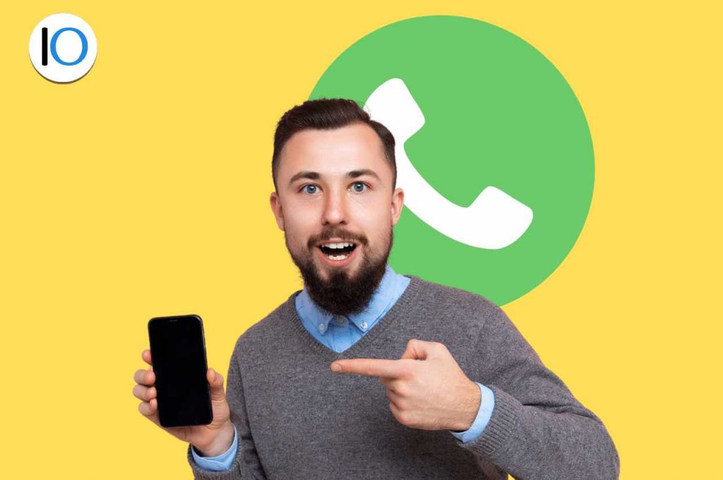 Uomo che indica telefono con logo whatsapp alle spalle