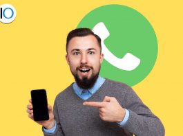 Uomo che indica telefono con logo whatsapp alle spalle