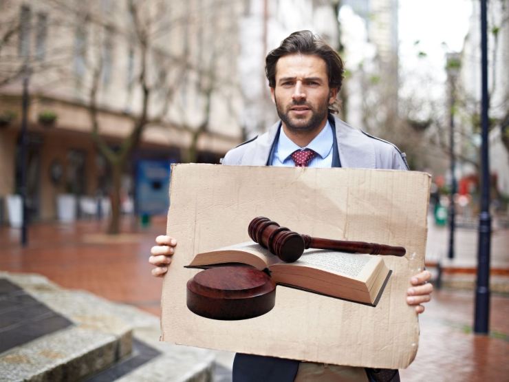 uomo con cartellone in mano con su il martelletto e il libro della legge