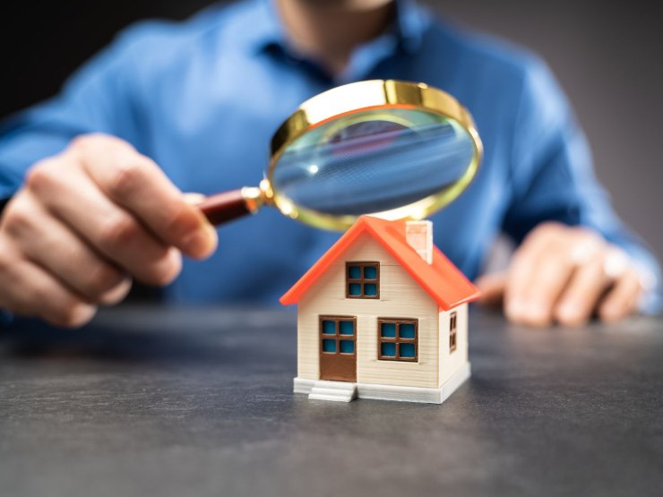 Uomo che con una lente di ingrandimento guarda una casa