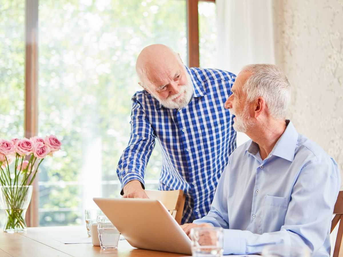 Due uomini anziani sorridenti che leggono al pc