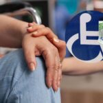 Mano una sull'altra e logo sedia a rotelle con soldi in euro