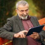 Uomo anziano seduto su una panchina con in mano un tablet