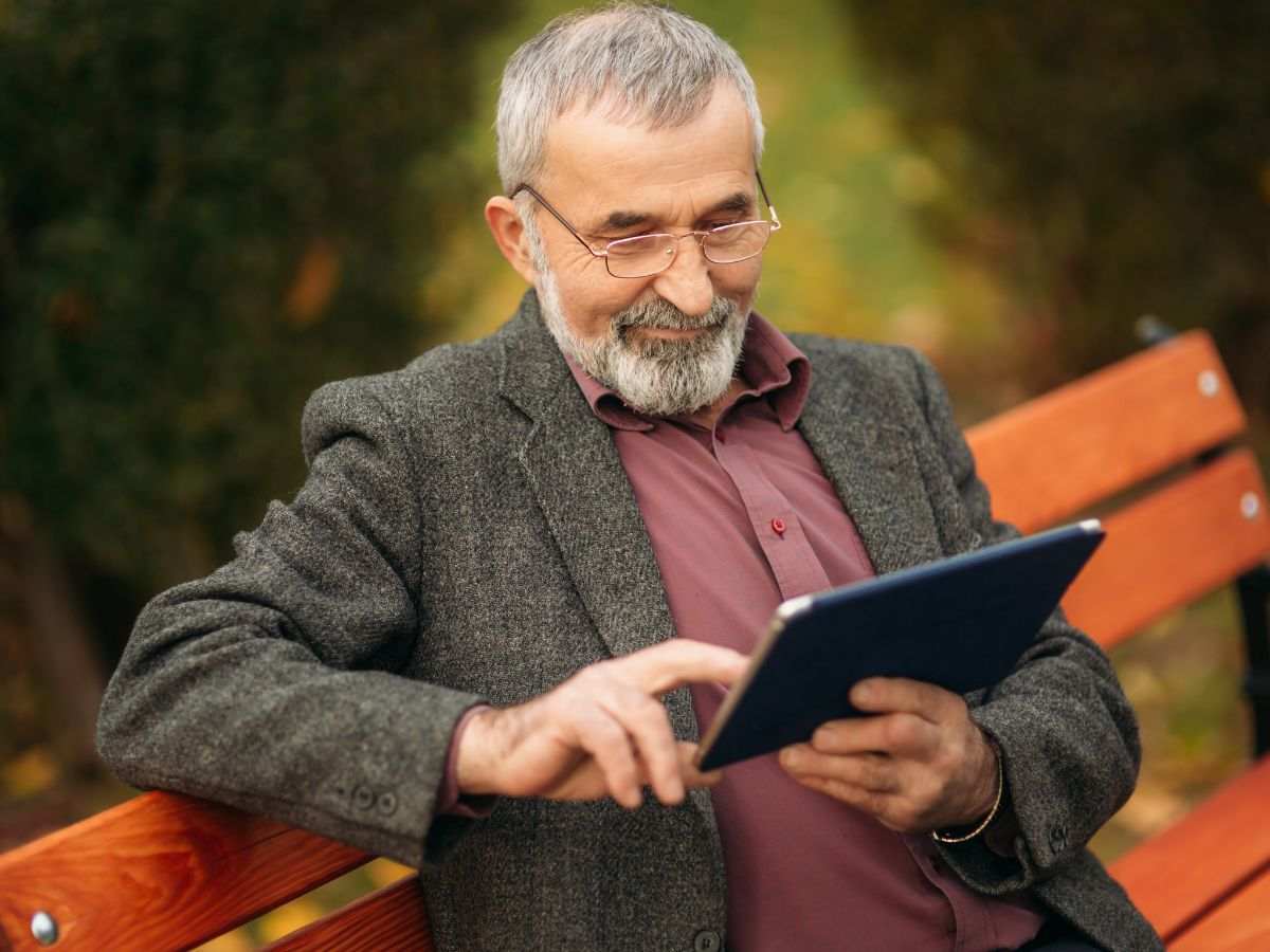 Uomo anziano seduto su una panchina con in mano un tablet