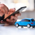 mani con smartphone e modellino auto