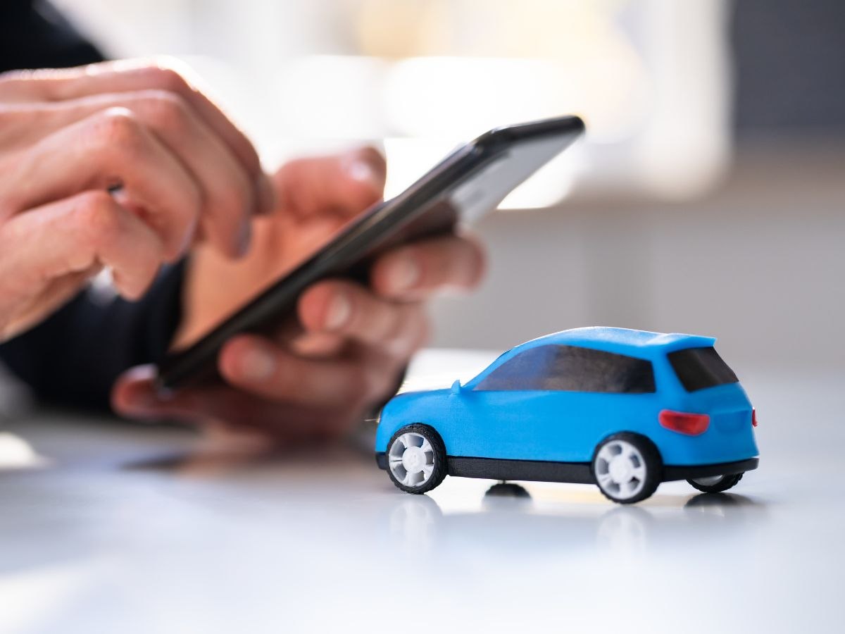 mani con smartphone e modellino auto