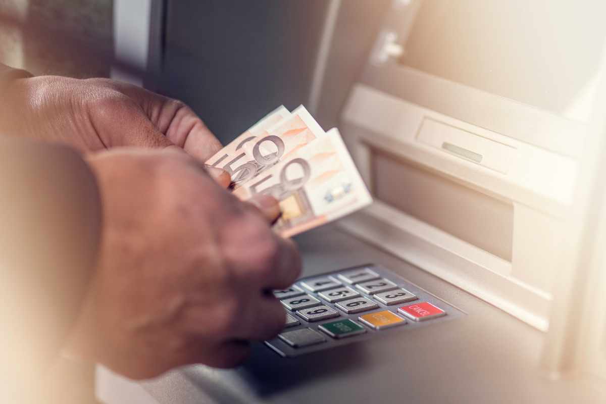 Persona che conta banconote da 50 euro davanti al bancomat