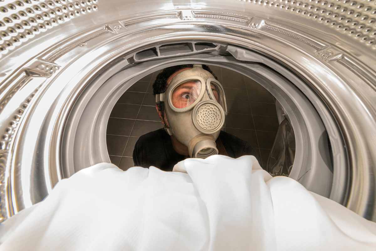 Persona con la maschera guarda dentro una lavatrice