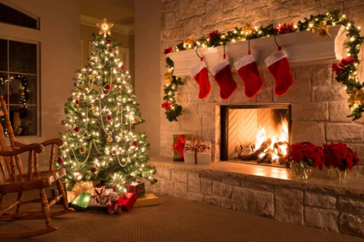 albero di natale illuminato in salotto accanto al caminetto