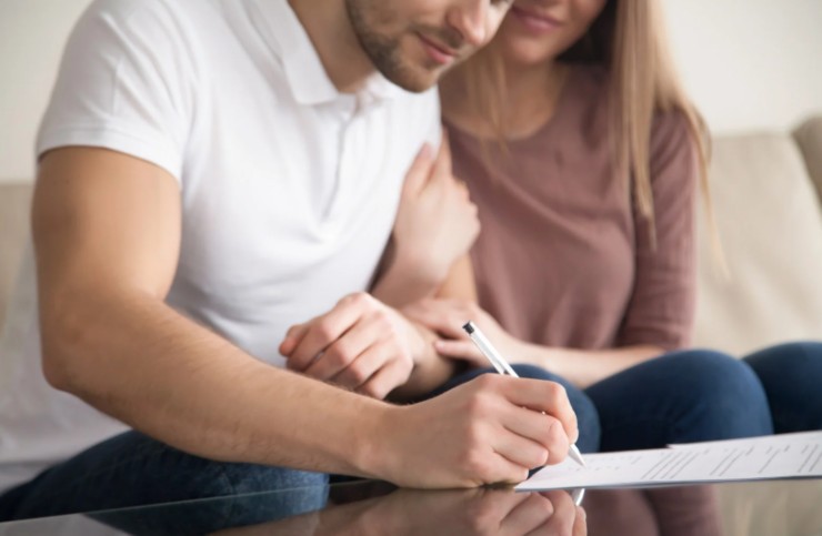 uomo che firma un contratto e accanto a lui una donna