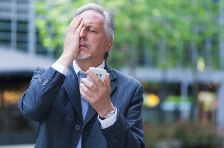 uomo disperato con una mano sulla faccia e il cellulare nell'altra mano