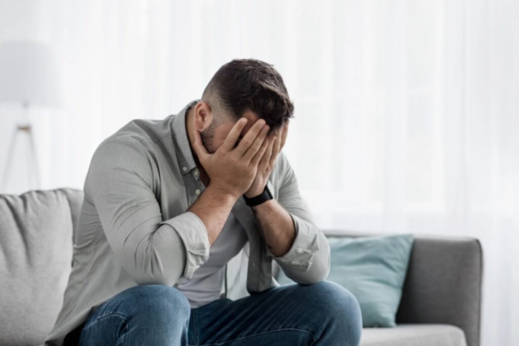 uomo disperato seduto sul divano con le mani sulla faccia
