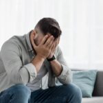 uomo disperato seduto sul divano con le mani sulla faccia