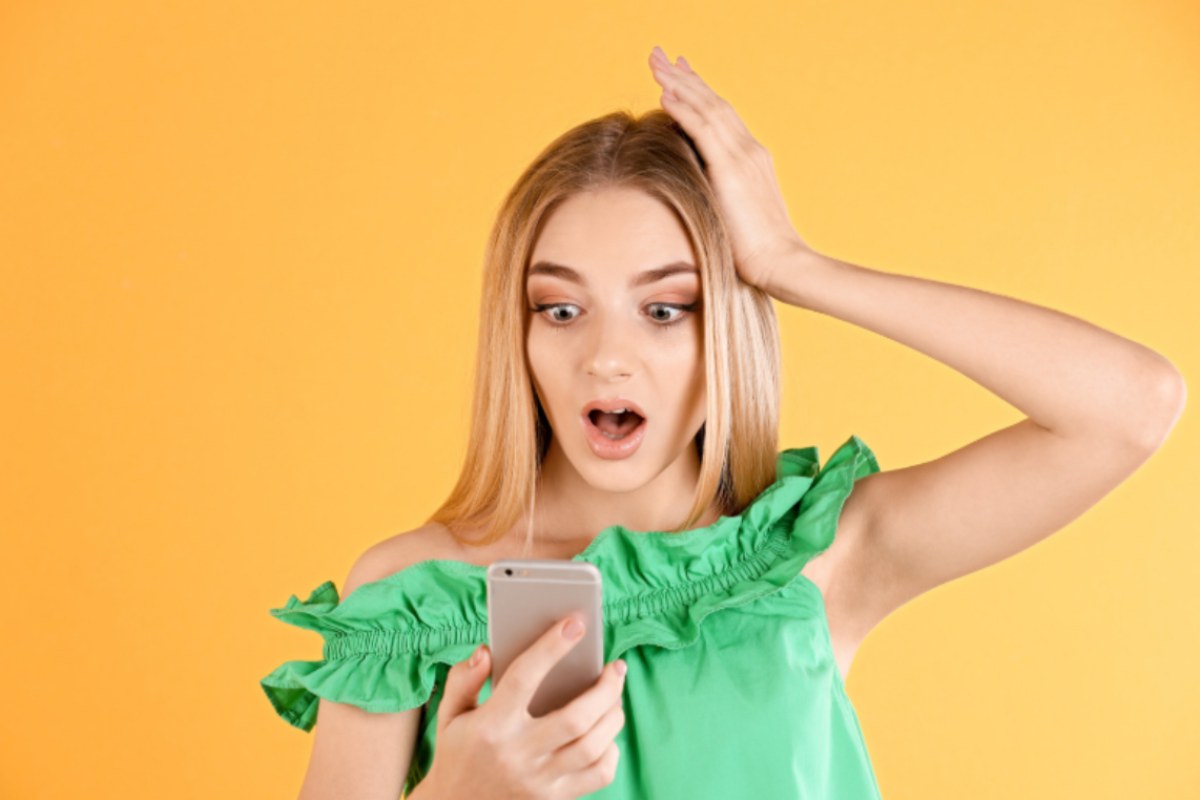 donna con espressione scioccata con in mano il cellulare 