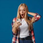 donna con espressione scioccata con la bocca aperta mentre guarda il cellulare