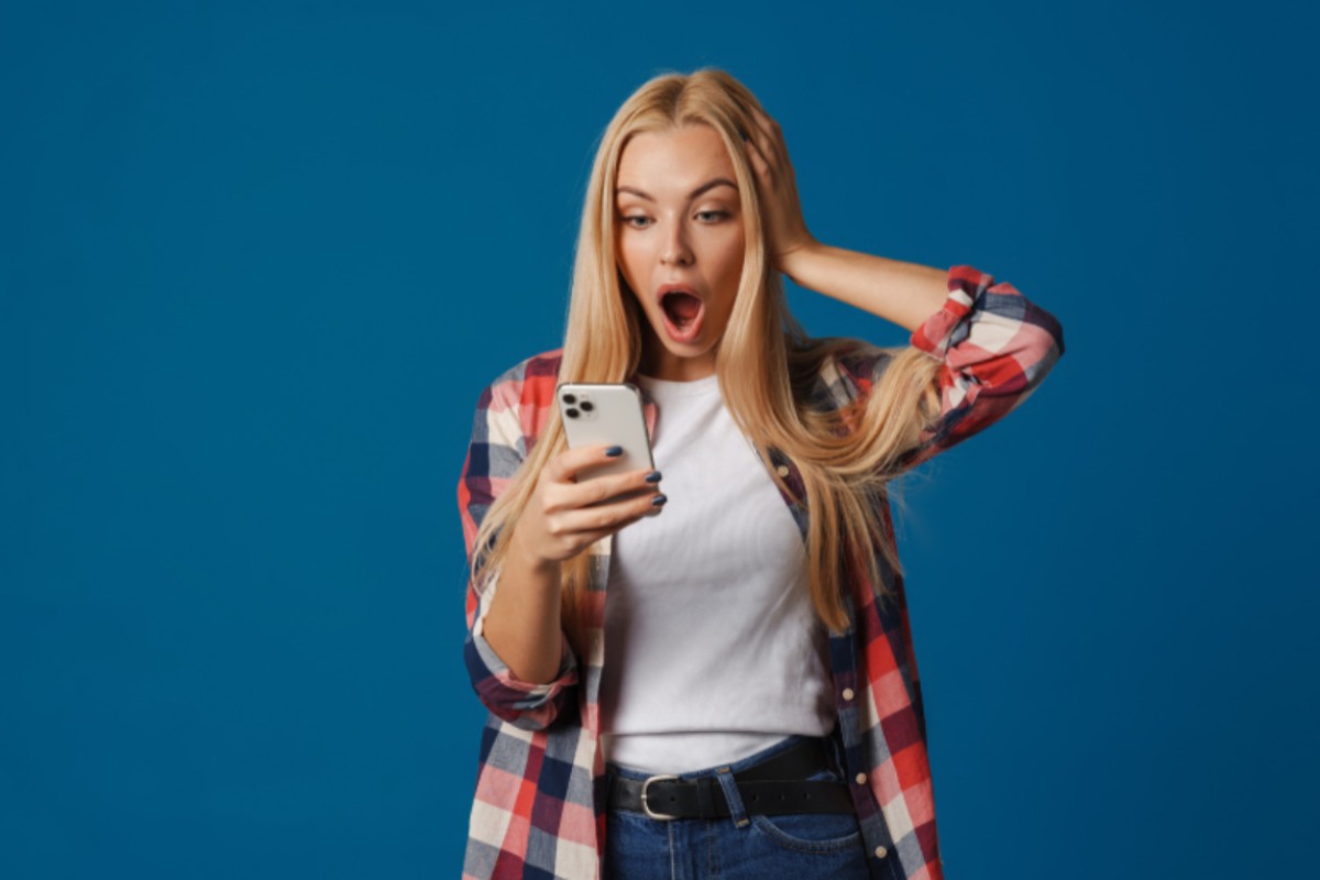 donna con espressione scioccata con la bocca aperta mentre guarda il cellulare
